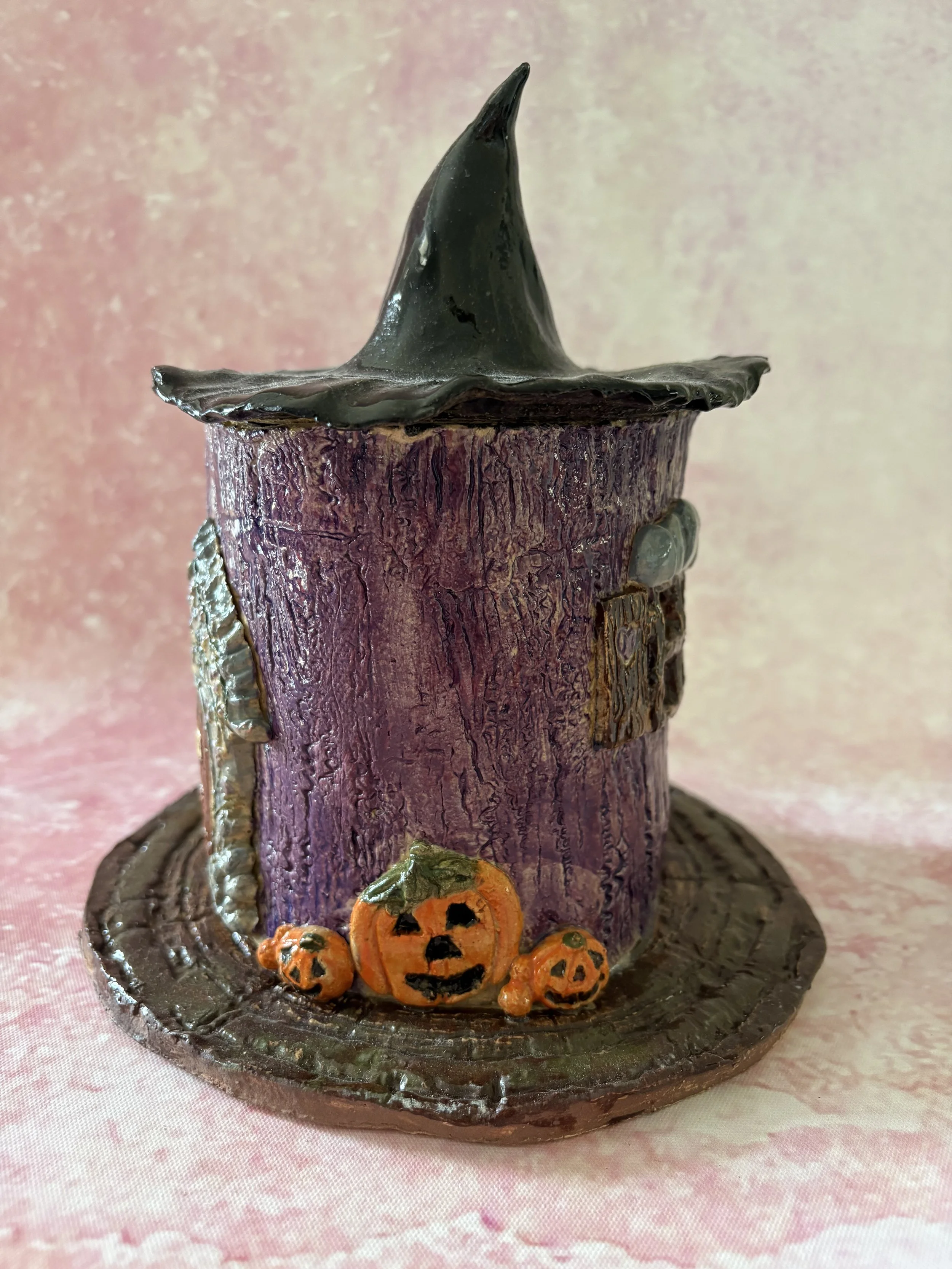 Purple witches cottage, with orange pumpkins to the right of the door.