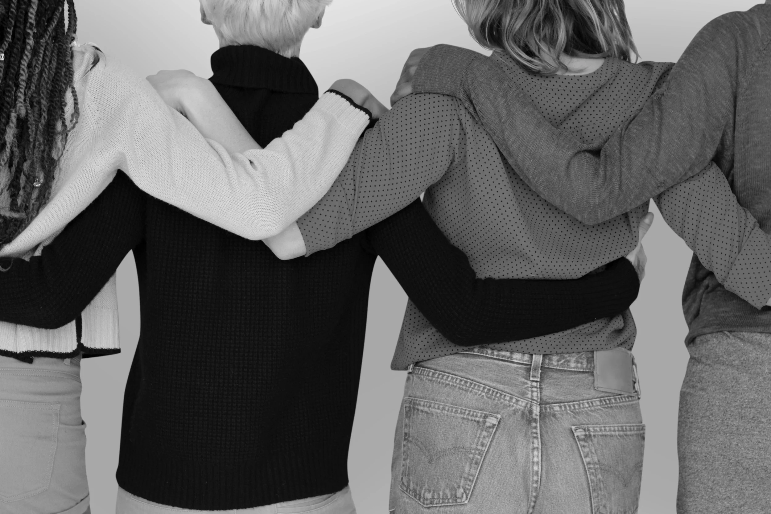 Group of four people standing with arms around each other, seen from the back, wearing casual clothing.