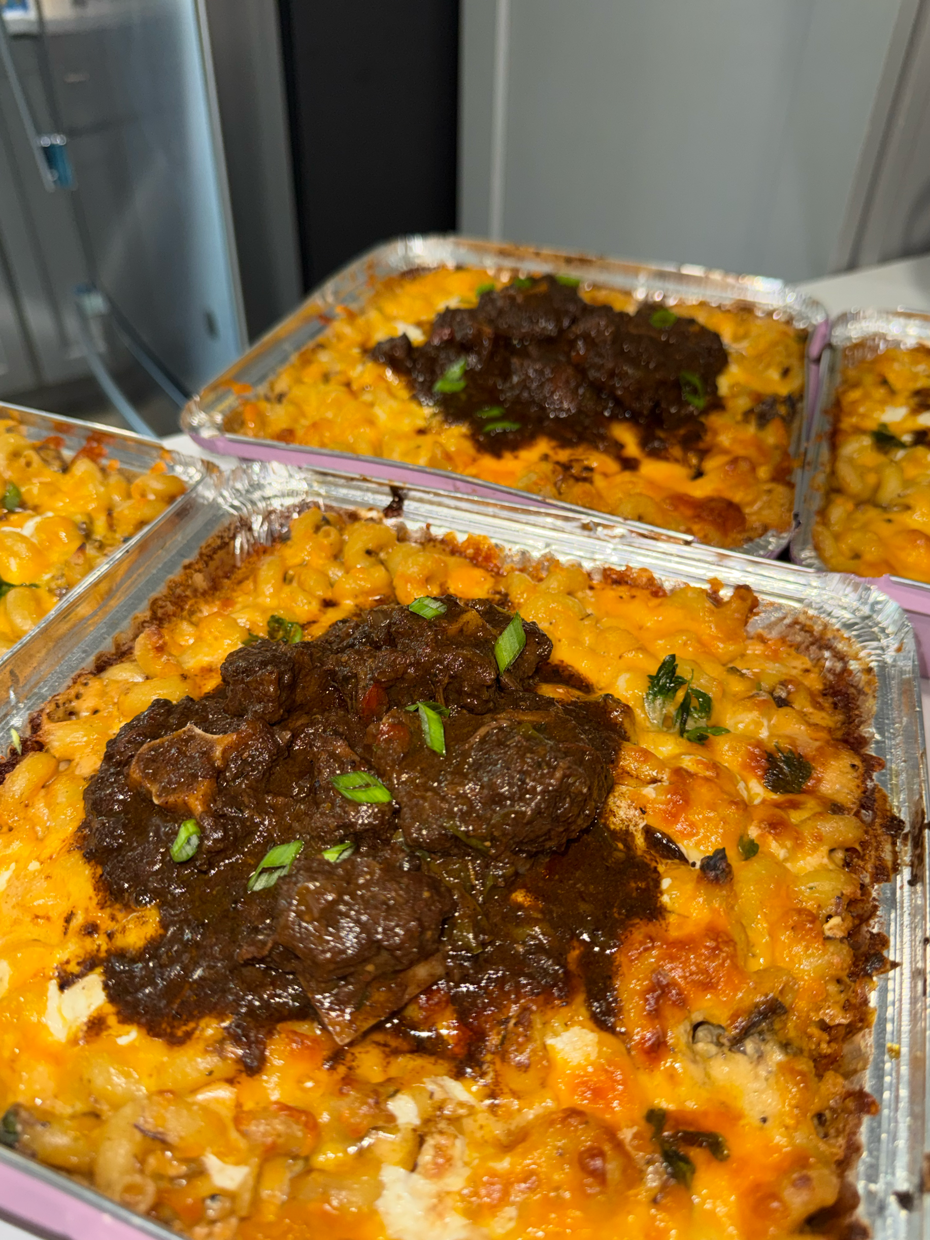 Close-up of three dishes of baked casserole with melted cheese, ground meat, and vegetables in aluminum containers.