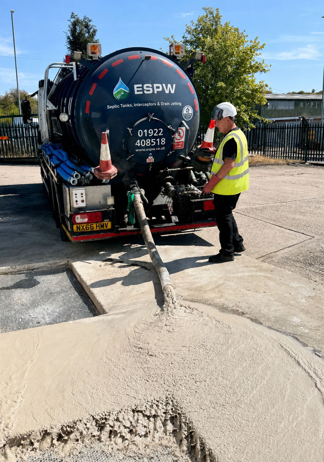 A worker in a yellow safety vest and helmet is operating a large sewer jetting truck labeled ESPW that is spraying water into a drainage grate to clean out a clogged sewer or drain.