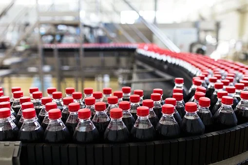 Rows of bottled Coca-Cola on a conveyor belt in a factory.