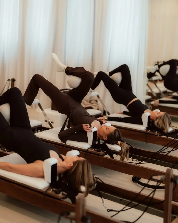 Trois femmes faisant de l'exercice sur des appareils de Pilates Allongées sur des tables, en position de récupération, dans une salle lumineuse.