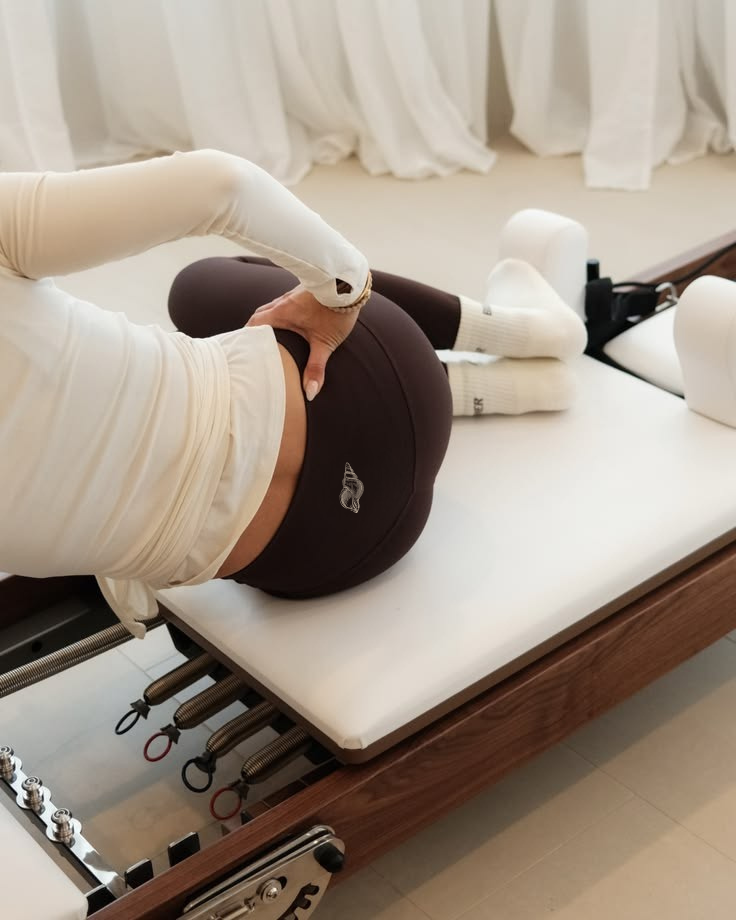 Une personne réalise un exercice de physiothérapie ou de yoga sur une table, en appui sur le côté et tenant sa cuisse, à côté de divers appareils de physiothérapie.
