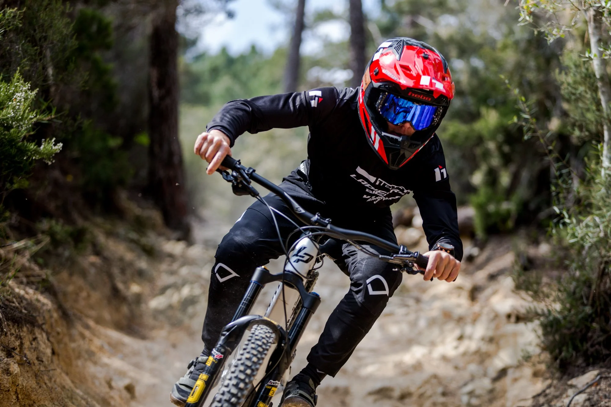 Un uomo in corsa con una mountain bike attraverso un sentiero boschivo, indossa un casco rosso e un completo nero