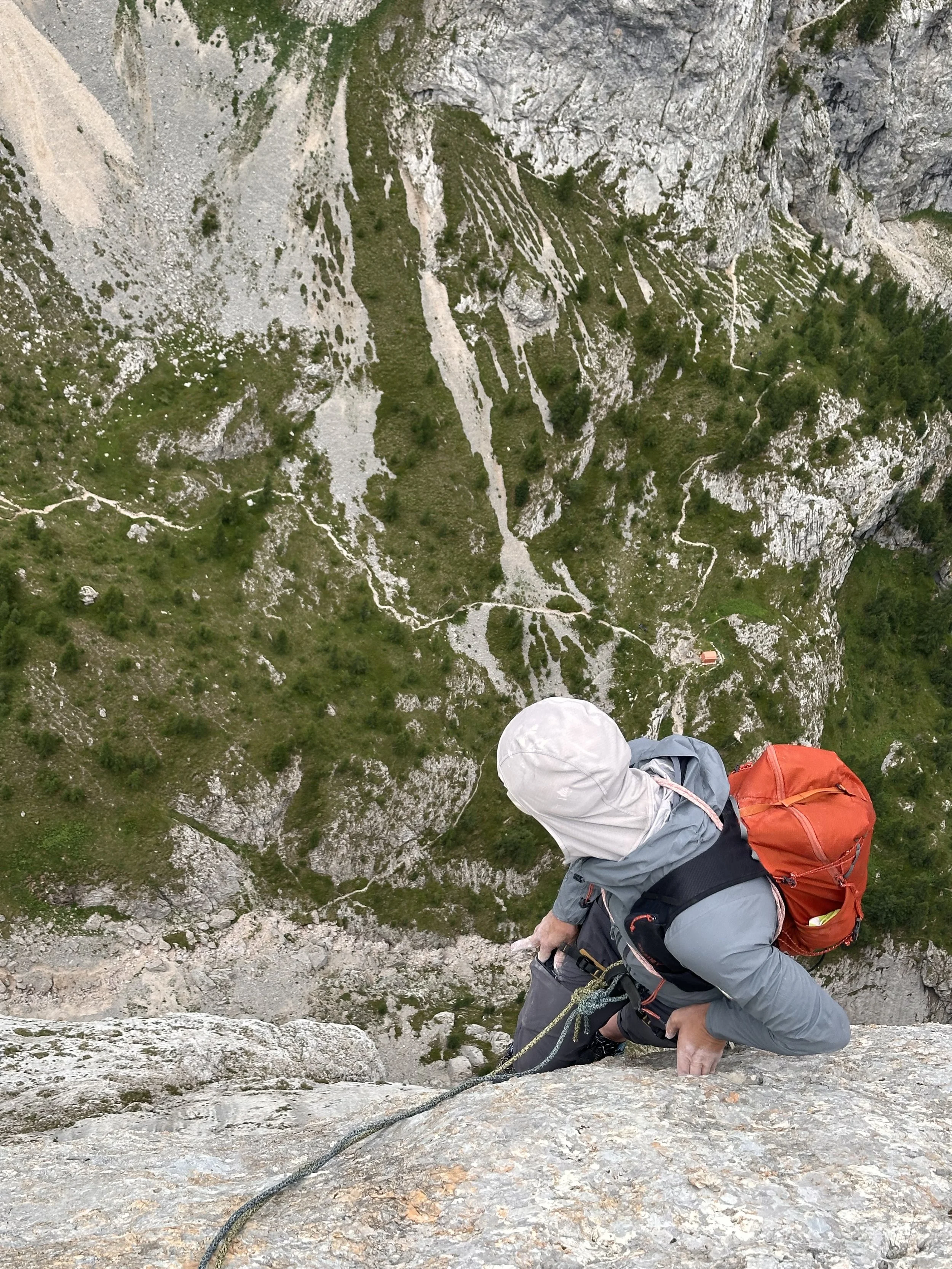 Persona che scala una parete di roccia mentre è legata a una corda di sicurezza, durante una salita multipich di arrampicata