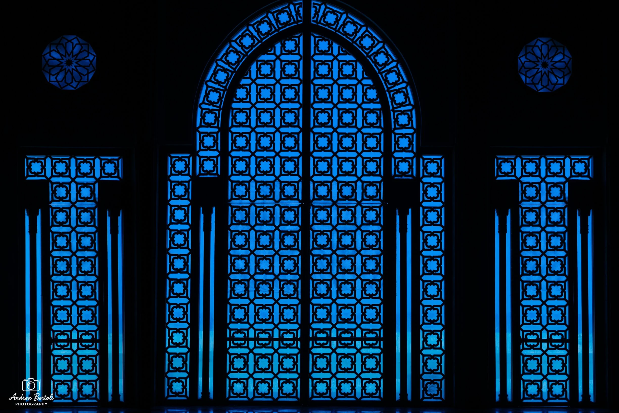 Vetrata blu decorativa con motivi geometrici e fiorellini all'interno della moschea Hassan II, composta da pannelli e due rosoni laterali.