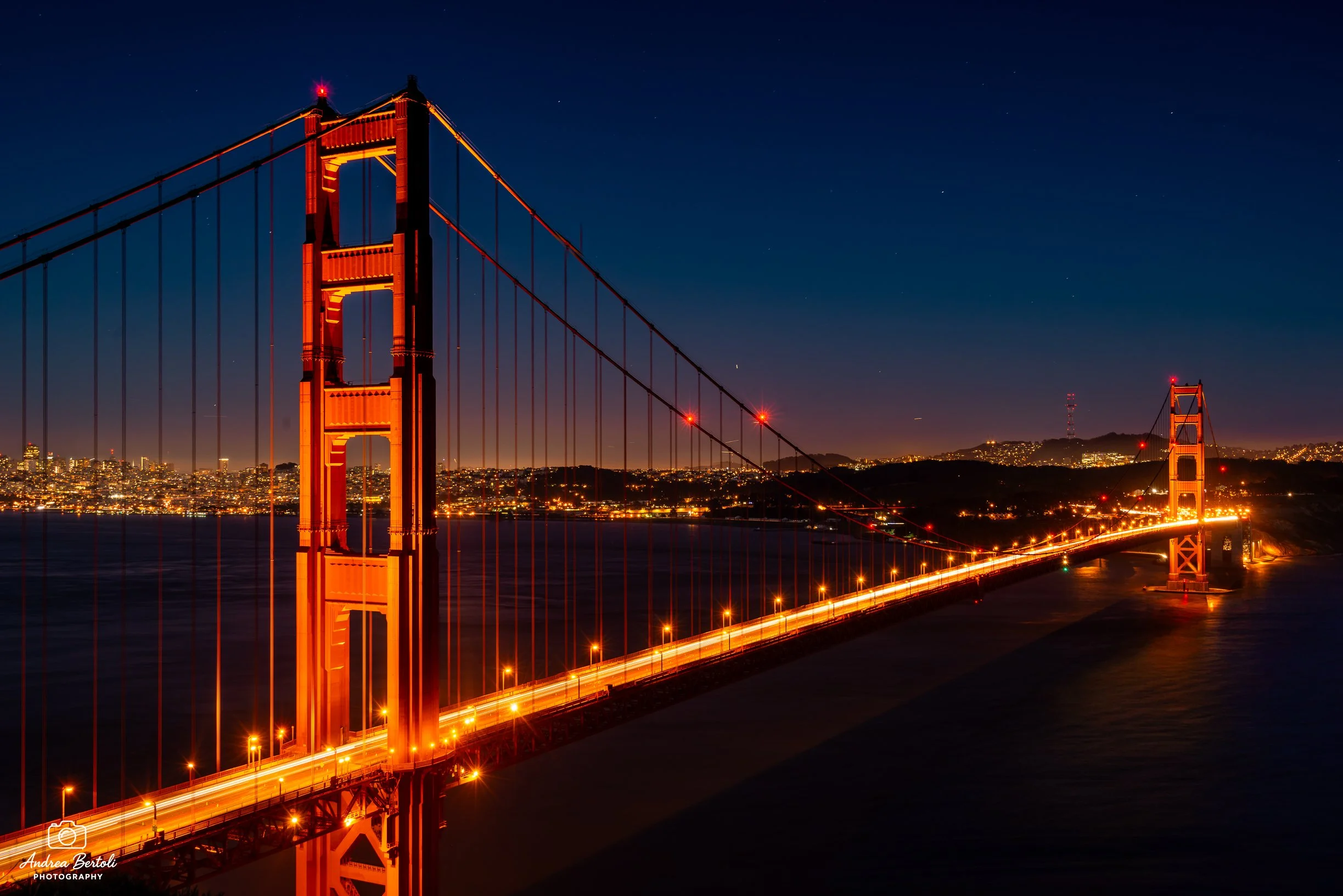 Il Golden Gate Bridge illuminato di rosso di notte con la città di San Francisco sullo sfondo e il cielo stellato sopra.