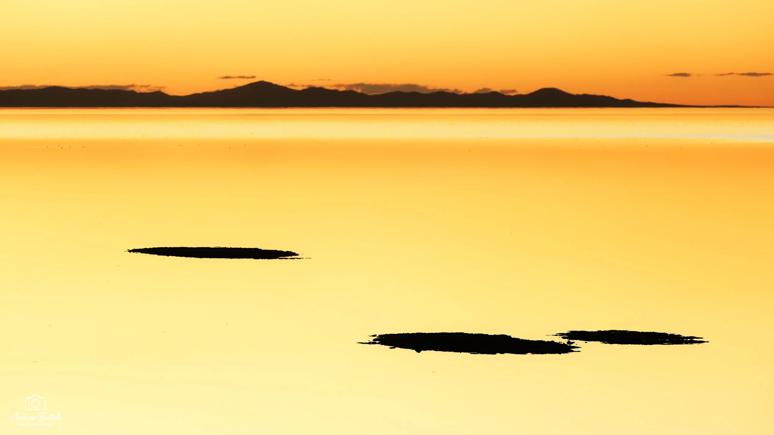 Tramonto su un lago con montagne sullo sfondo, acqua riflettente i colori del cielo, con alcune aree di ombra o riflesso buio ad Antelope Island.