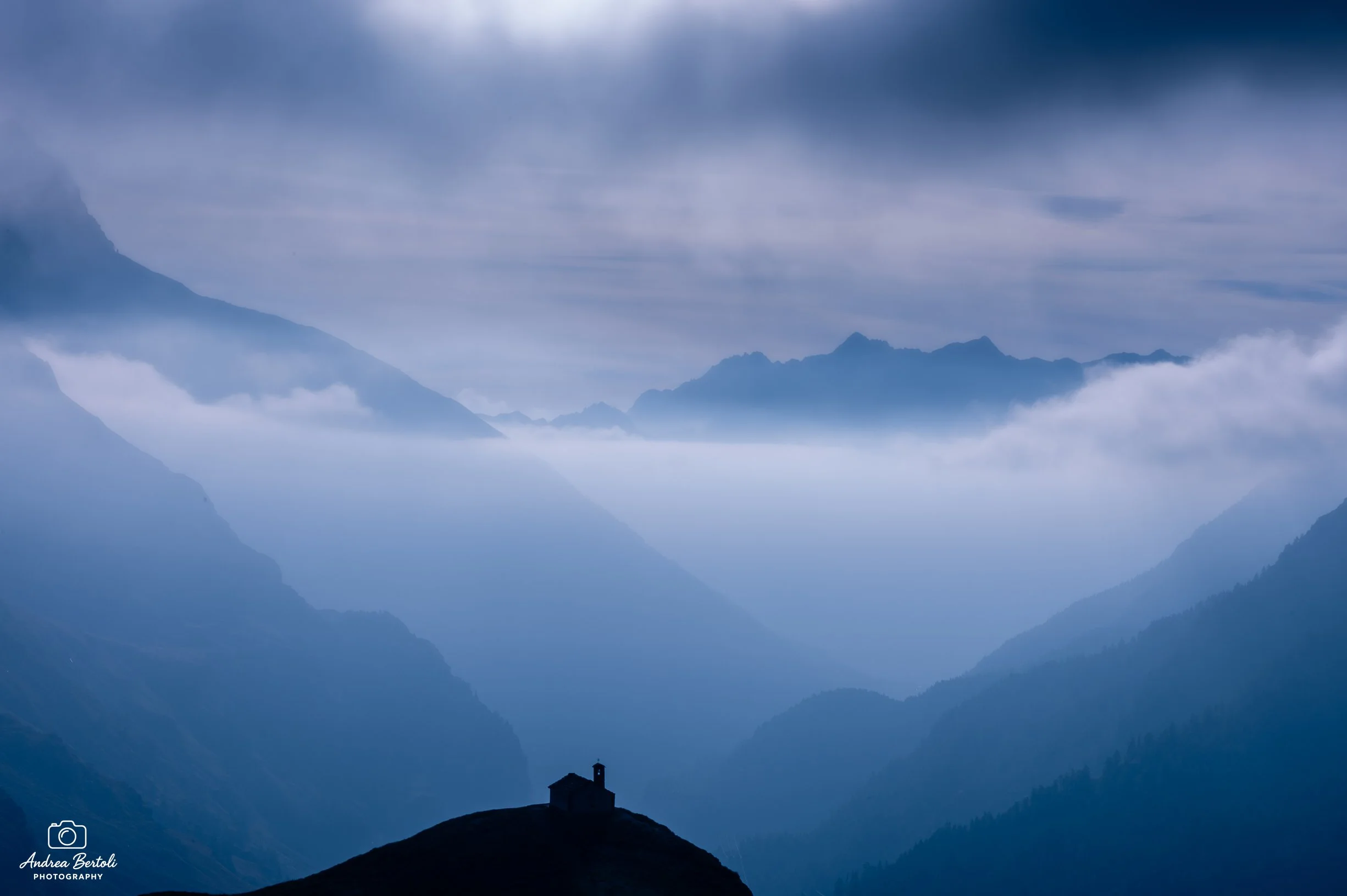 Montagne avvolte dalla nebbia con la Chiesa Madonna della Neve e Pian del Nivolet in primo piano su una collina