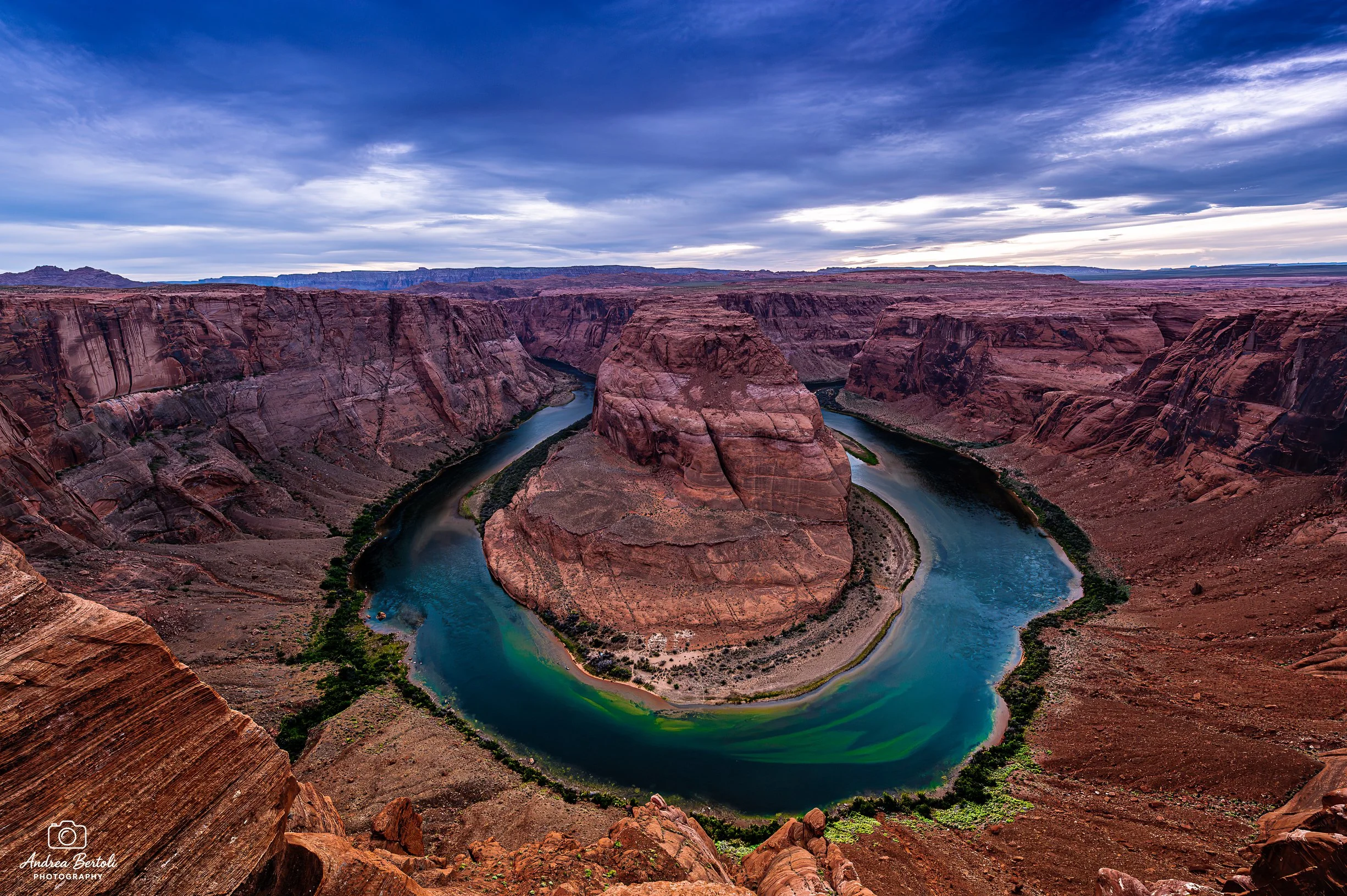 Una vista panoramica dell'Horseshoe Band con il Fiume Colorado che si snoda tra le pareti rocciose rosse e marroni sotto un cielo nuvoloso.