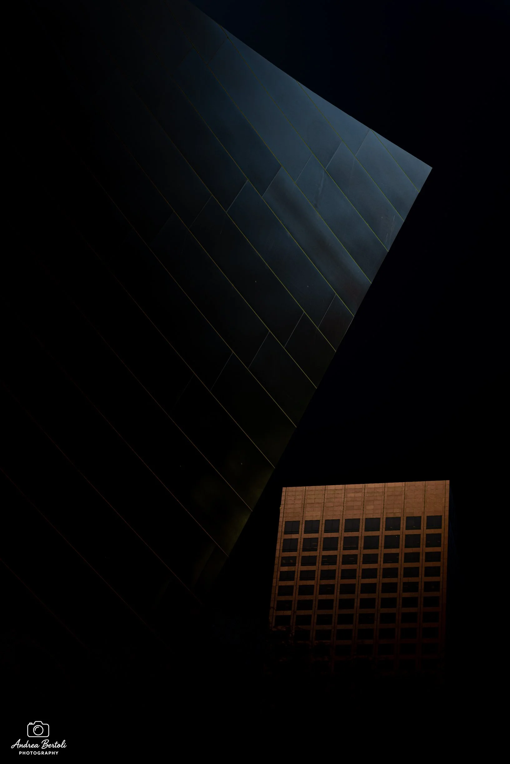 Immagine di un edificio alto con una facciata di vetro e un'altra di mattoni, scattata di notte con alcune luci accese.
