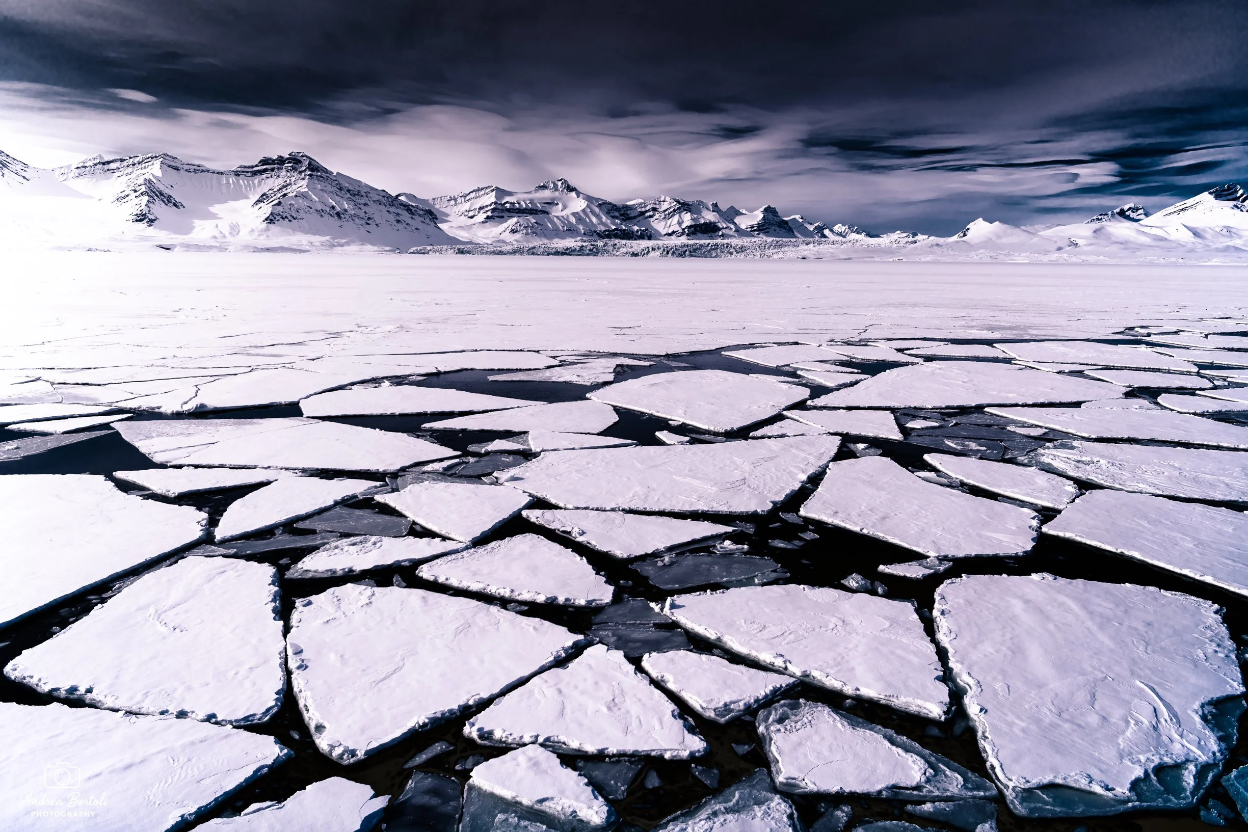 Paesaggi artici con montagne innevate sullo sfondo e lastre di ghiaccio spezzate sulla superficie di acqua congelata.