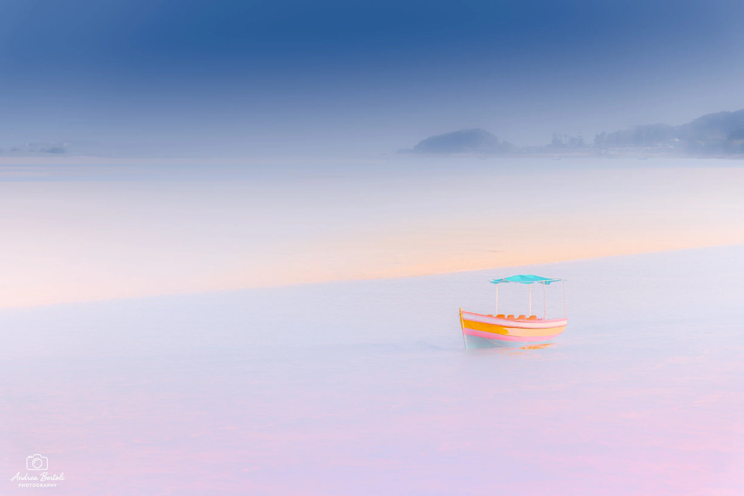 Una barca colorata sulla superficie calma di un lago o mare con sfondo di cielo e qualche collina o isola lontana a Oualidia in Marocco.