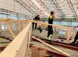 Arbetare i en byggnad under konstruktion, med träbalkar och byggmaterial runt omkring.