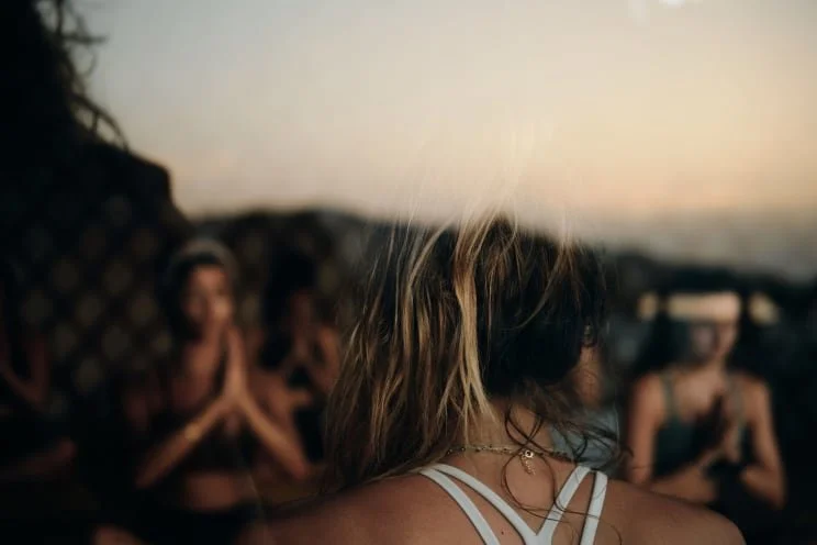 Group of women practicing yoga on a beach during sunset.