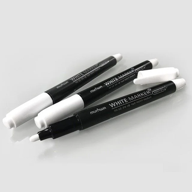 Three black markers with white caps on a white surface