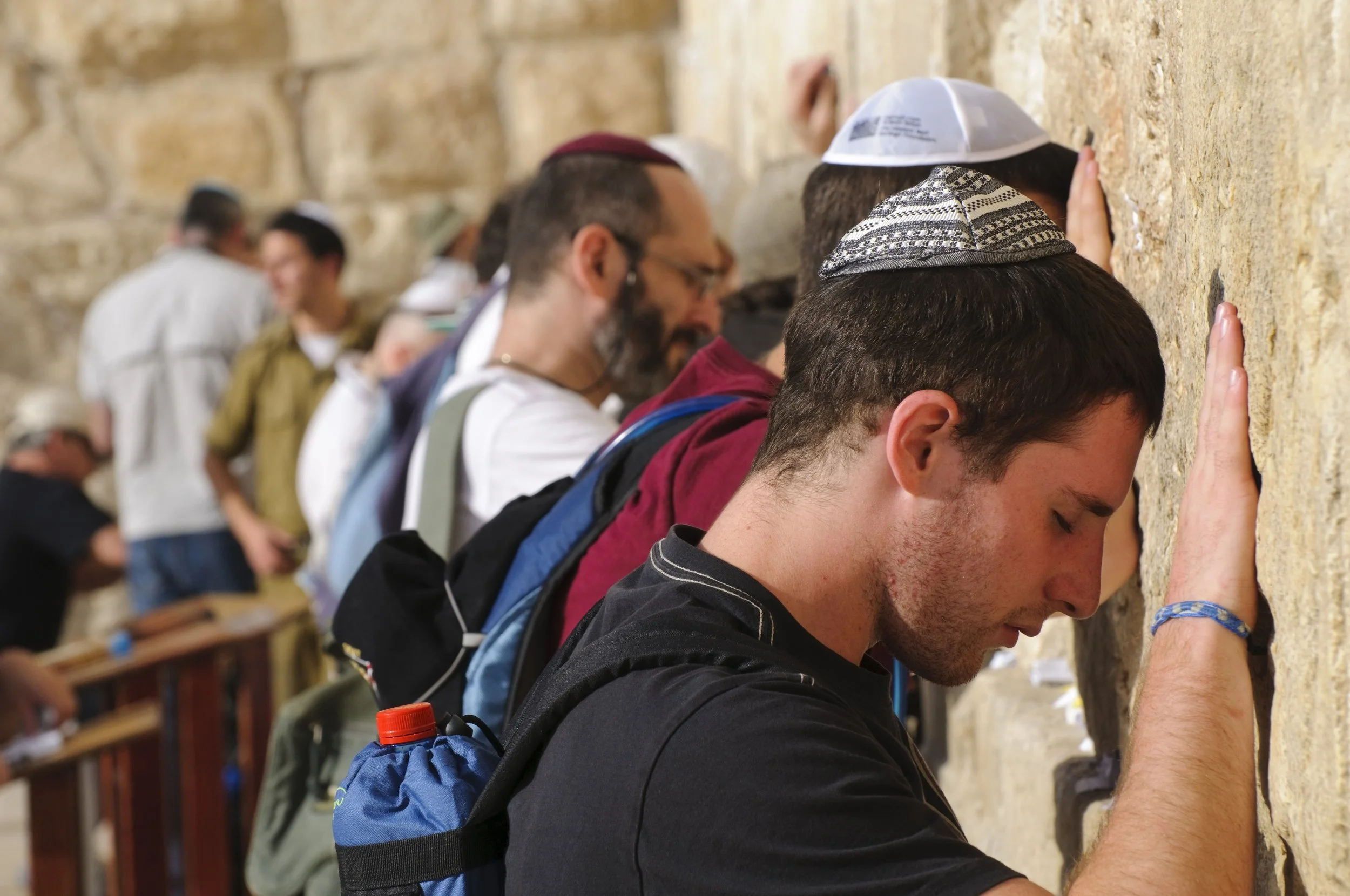 A group of men praying at the Western Wall, with their hands touching the wall and heads bowed in prayer.