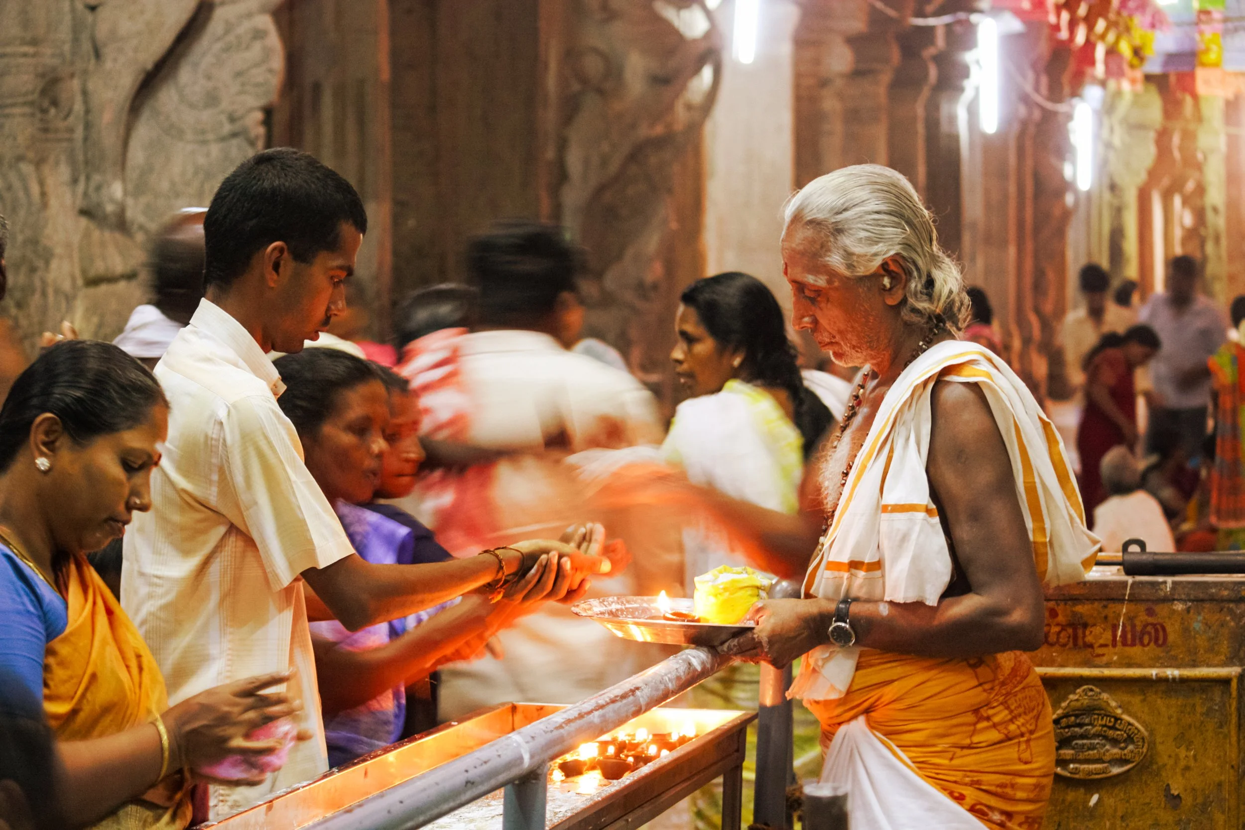 People participating in a religious or cultural ceremony, offering prayers or blessings at a temple or sacred site, with warm lighting and traditional attire.