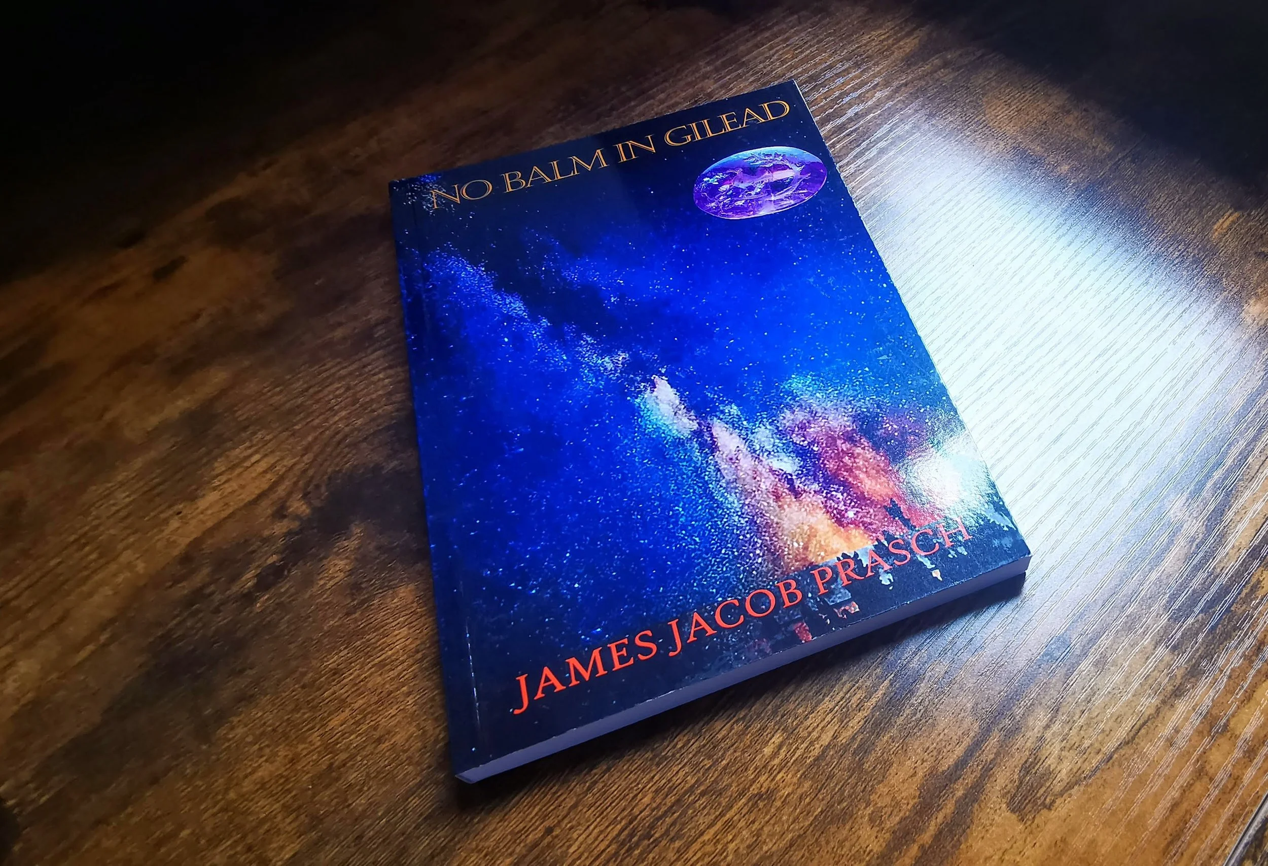 A science fiction book titled 'No Balm in Gilead' by James Jacob Prasch resting on a wooden surface, with a colorful cosmic or galaxy-themed cover.