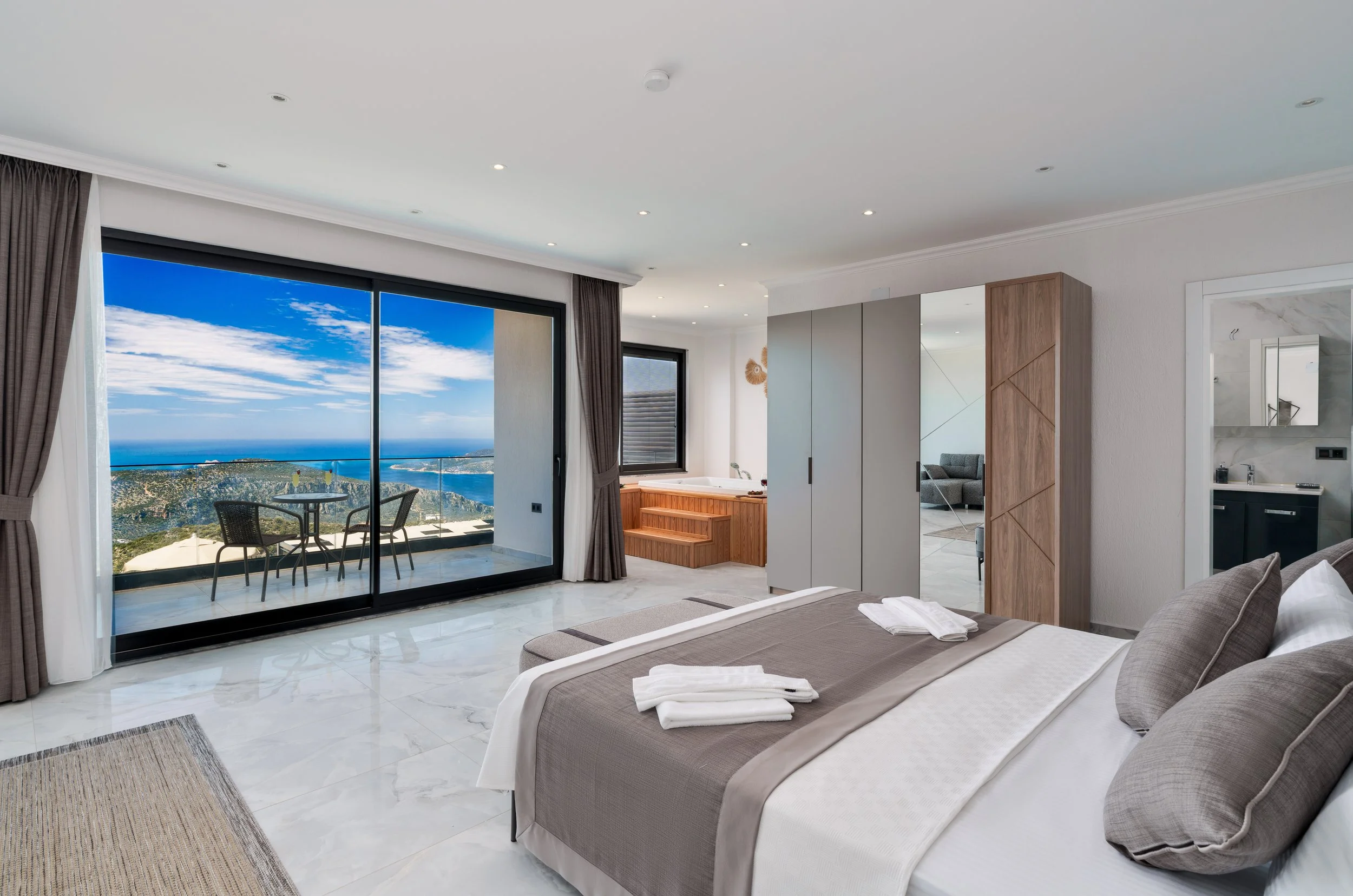 Modern bedroom with large sliding glass doors leading to a balcony with a view of the ocean and mountains.