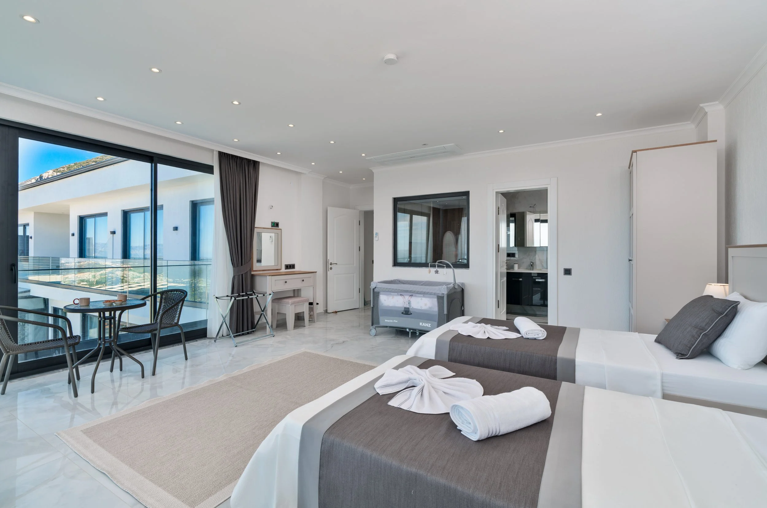 Hotel room with two beds, towels, a window, and balcony with outdoor seating.