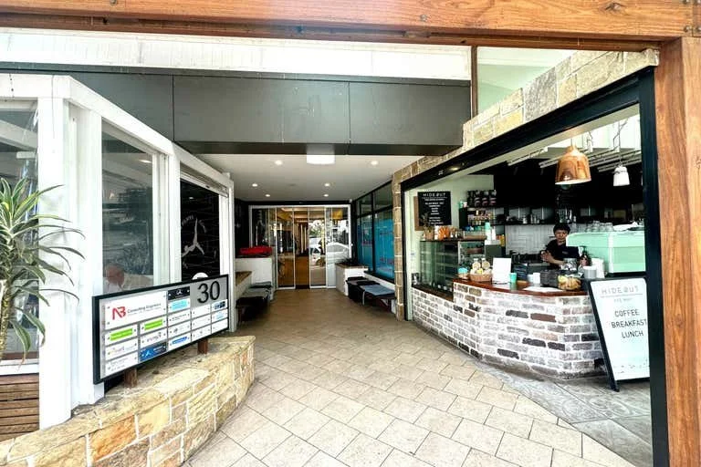 Entrance to a cafe or coffee shop with a seating area and a counter where orders are taken, featuring a brick exterior and a digital display.