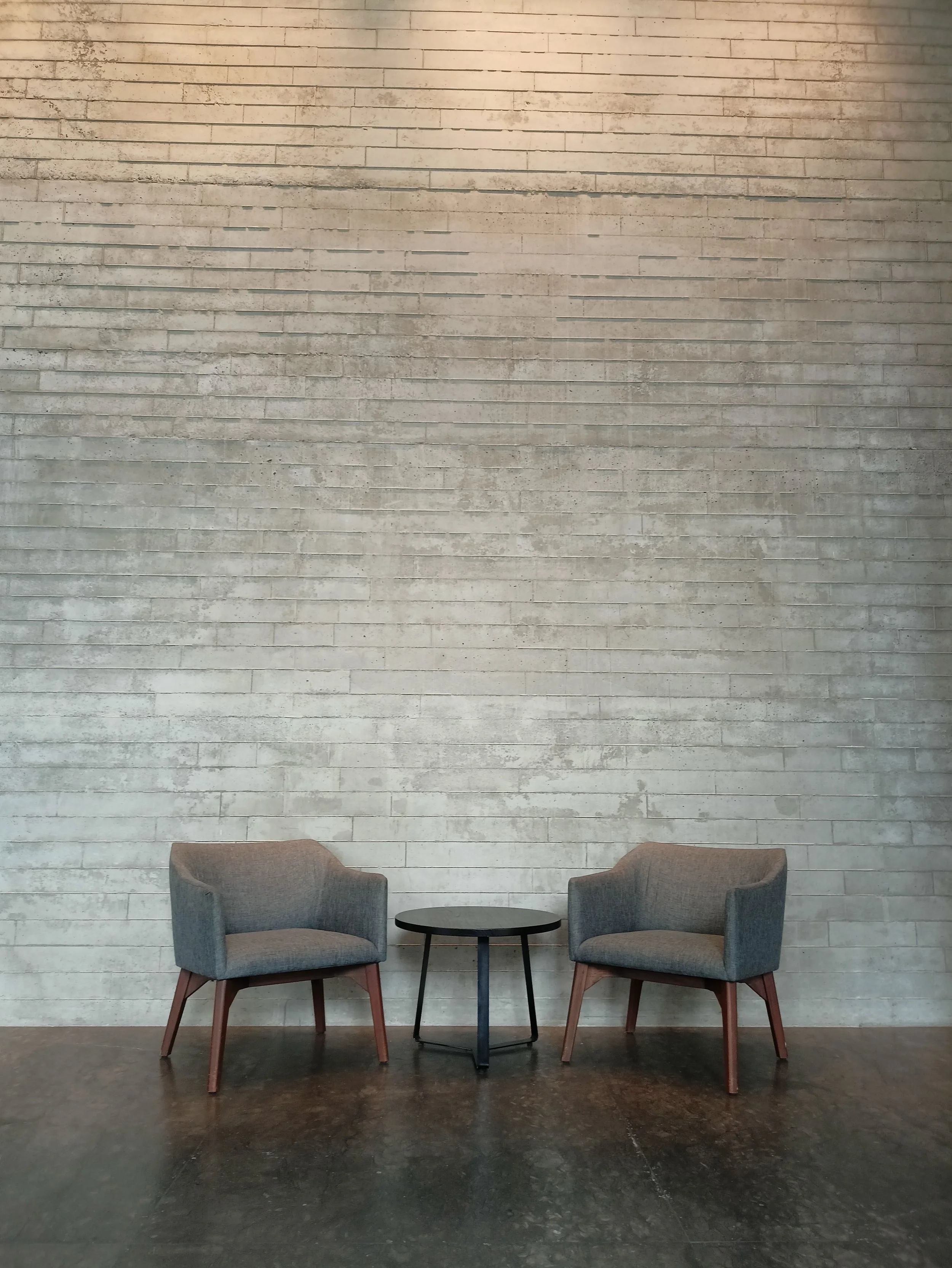 Two chairs, either side of a round coffe table, set against a high grey brick walll