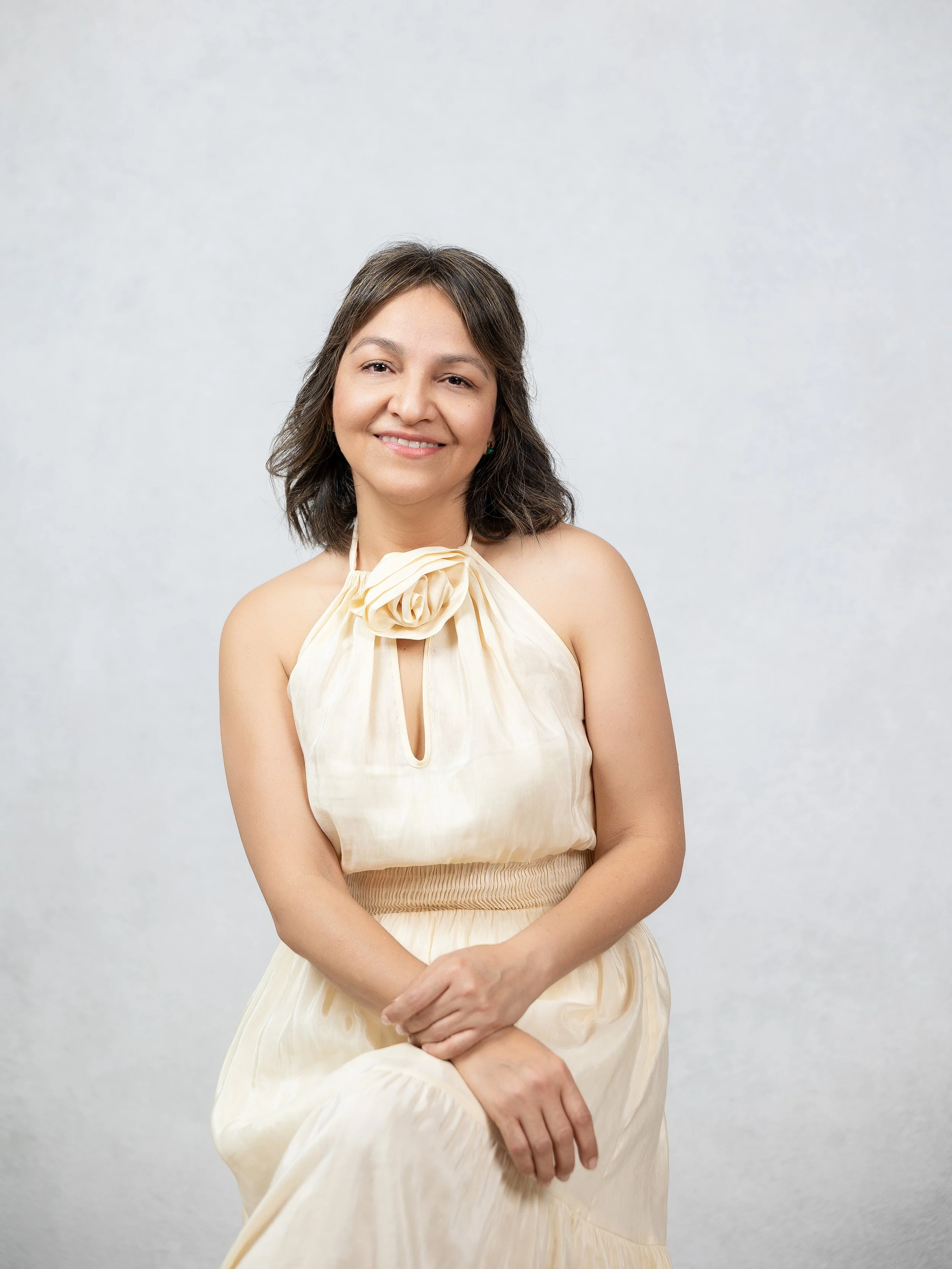 Mujer sonriendo, con vestido beige y fondo gris claro.
