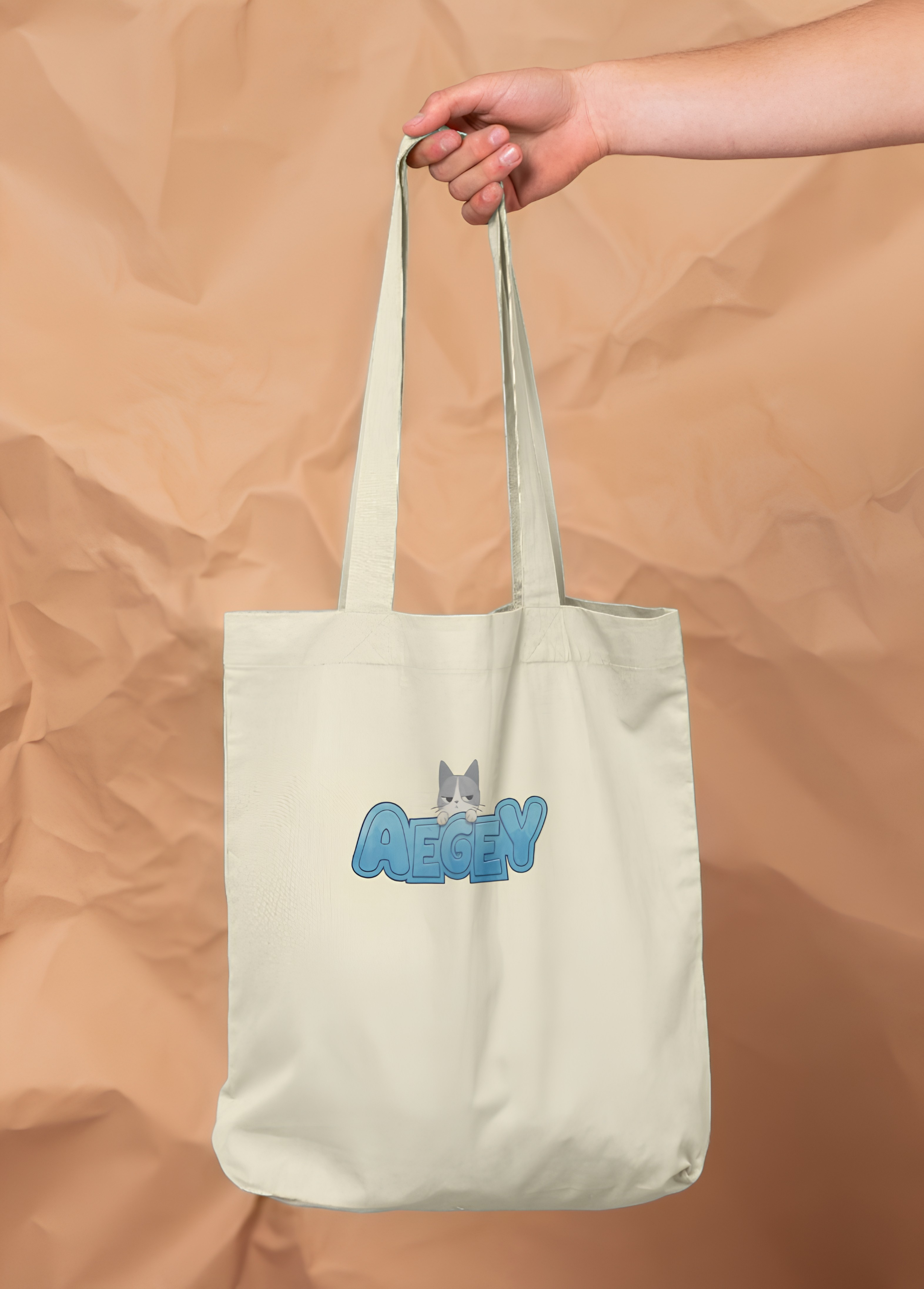 A white tote bag featuring 'Aegey' in blue letters, being held by a person's hand.