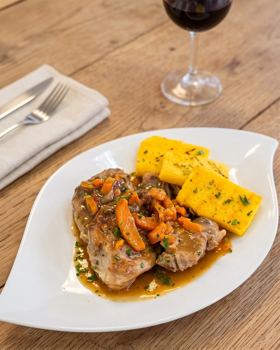 Poulet avec sauce aux carottes et accompagnement de polenta, servi dans une assiette blanche, avec verre de vin rouge, sur une table en bois.