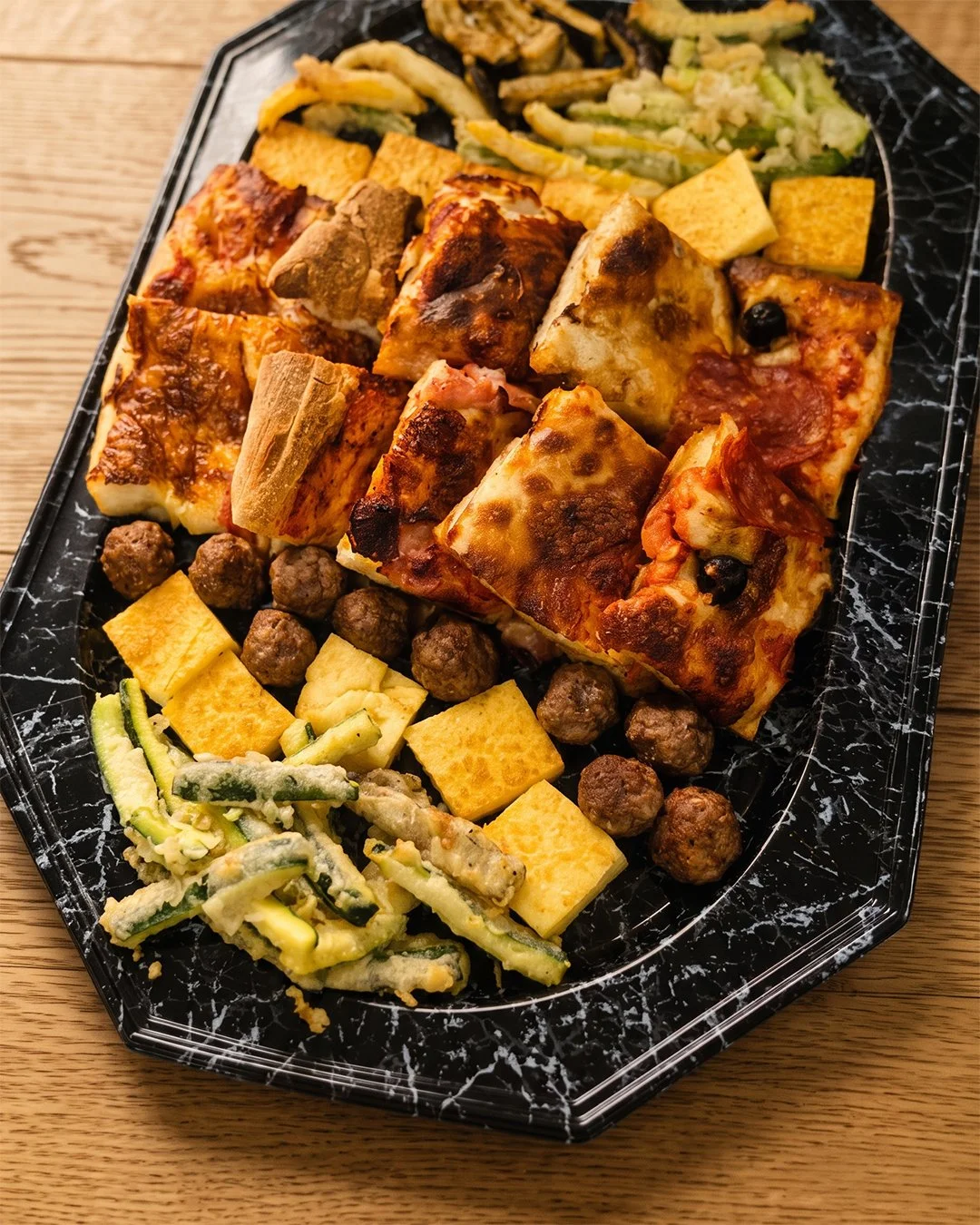 Assortiment de pizzas, boulettes de viande, légumes en tempura, œufs coupés, et morceaux de fromage sur un plateau.