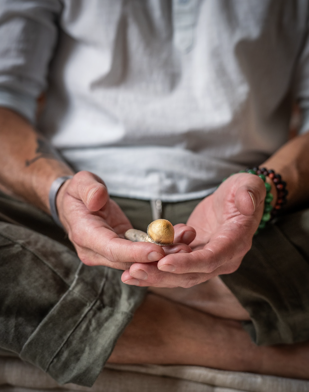 Person holding a small, round, gold-colored object in their hands, wearing bracelets, with a blurred background.