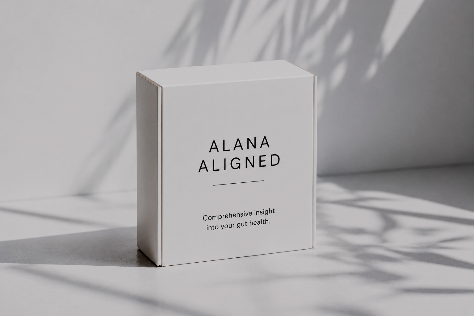 A white box with black text that reads 'ALANA ALIGNED' and 'Comprehensive insight into your gut health,' placed on a light surface with shadows of leaves in the background.