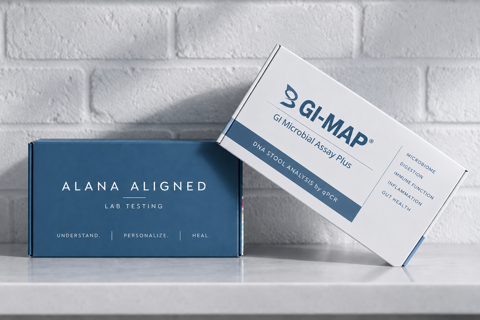 Two boxes on a white table in front of a brick wall. The left box is dark blue with white text that reads "ALANA ALIGNED LAB TESTING