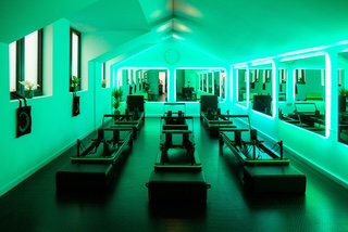 A room illuminated with green lighting, featuring multiple mirrors on one wall, bench seating, and a central lane with tables, creating a modern, minimalist space.