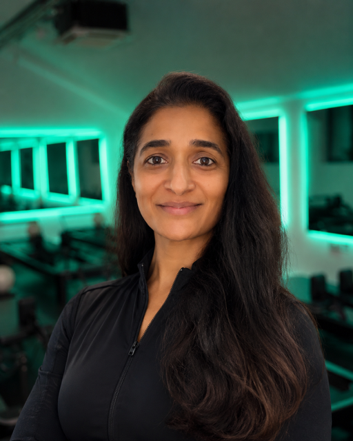 Portrait of a woman with long dark hair, smiling, in a room with green neon lights and computer desks.