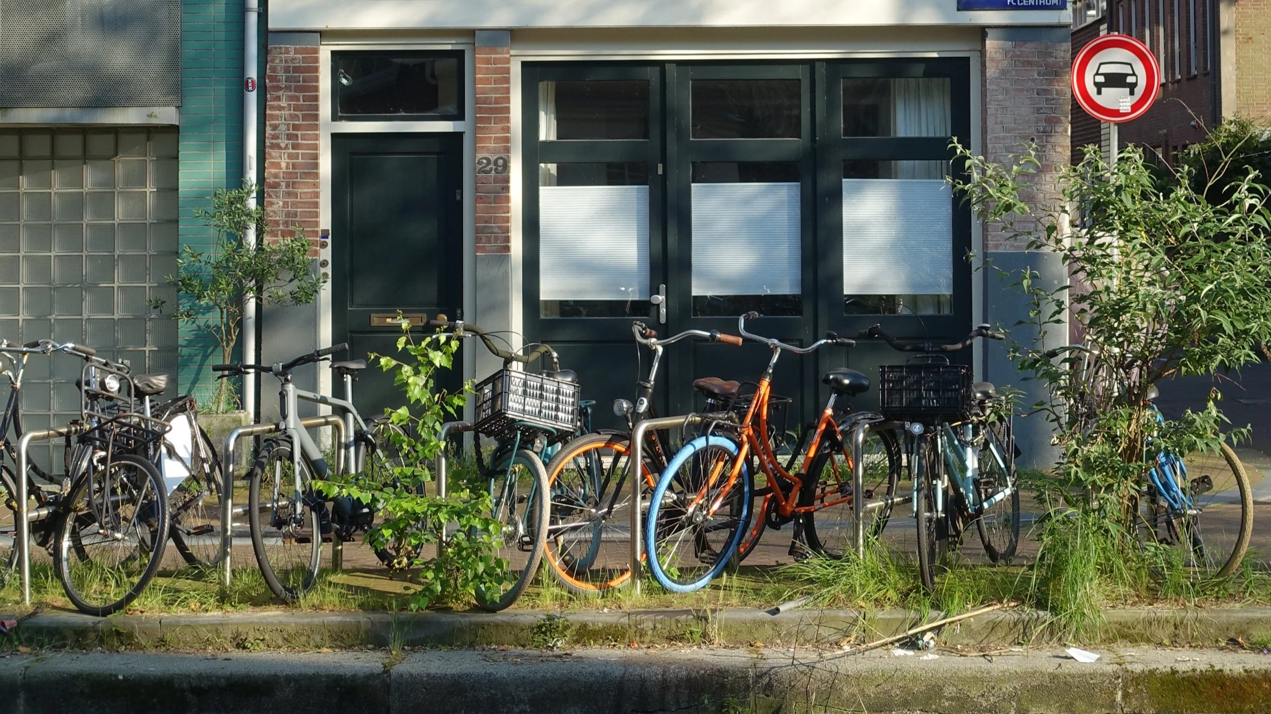 Several bicycles parked at bike racks outside a building with a dark green facade and brick walls.