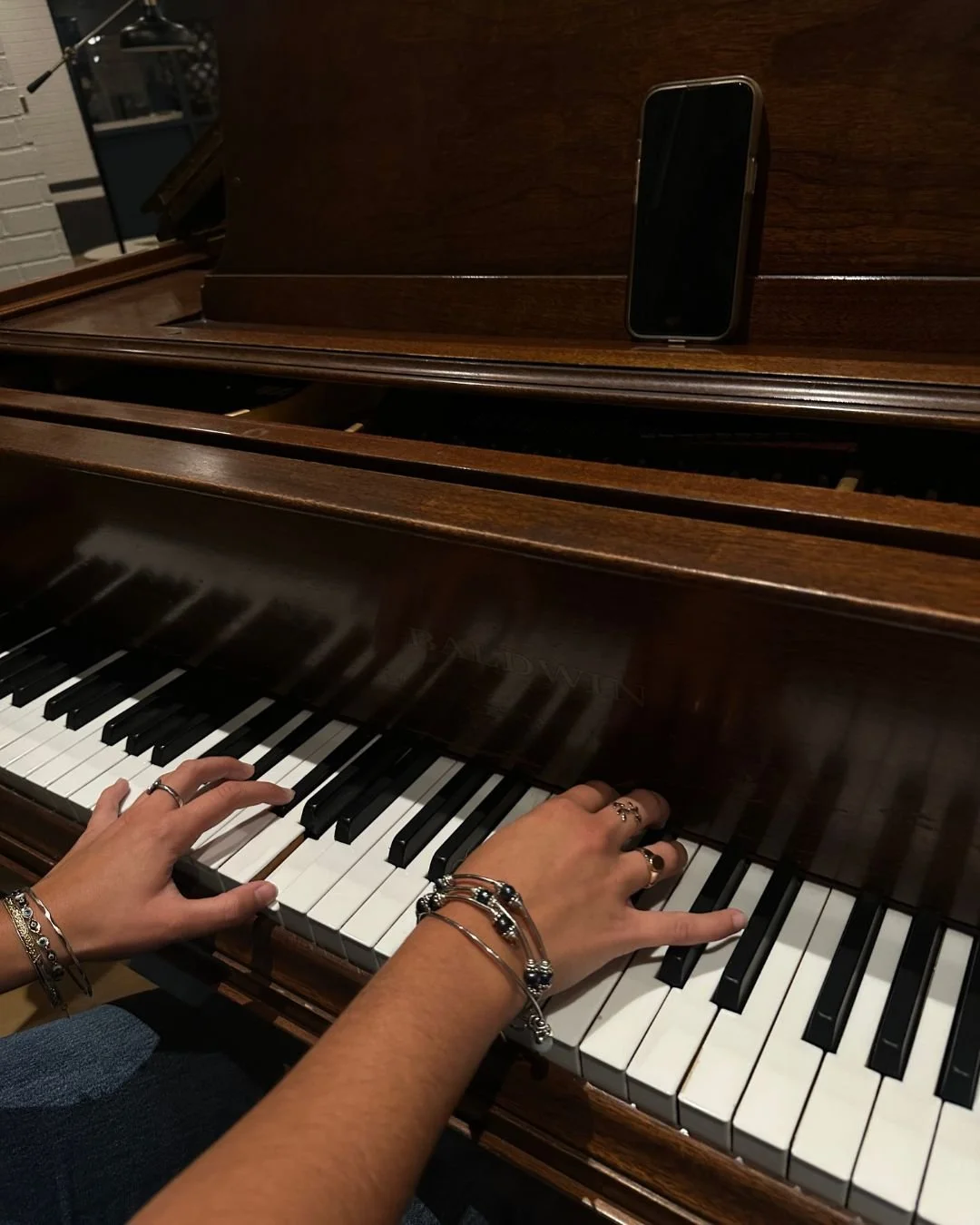 Person playing a brown upright piano with a smartphone placed on top of it.