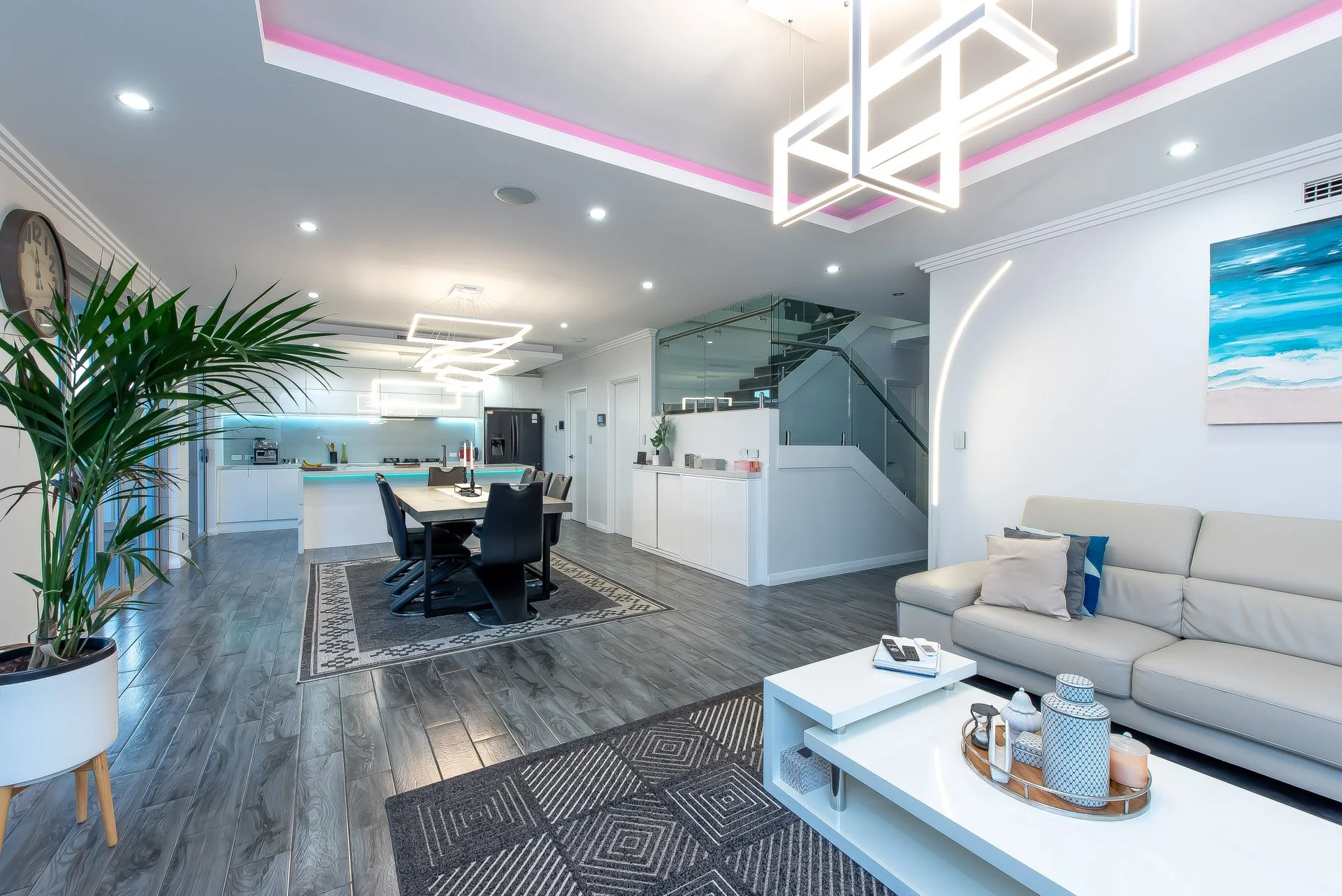 Modern open-concept living space with a dining area, kitchen, and seating. Includes a large houseplant, patterned rugs, and contemporary lighting fixtures.