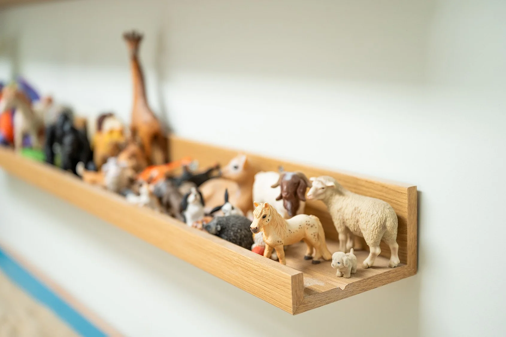 Collection of small farm animal figures displayed on a wooden shelf.