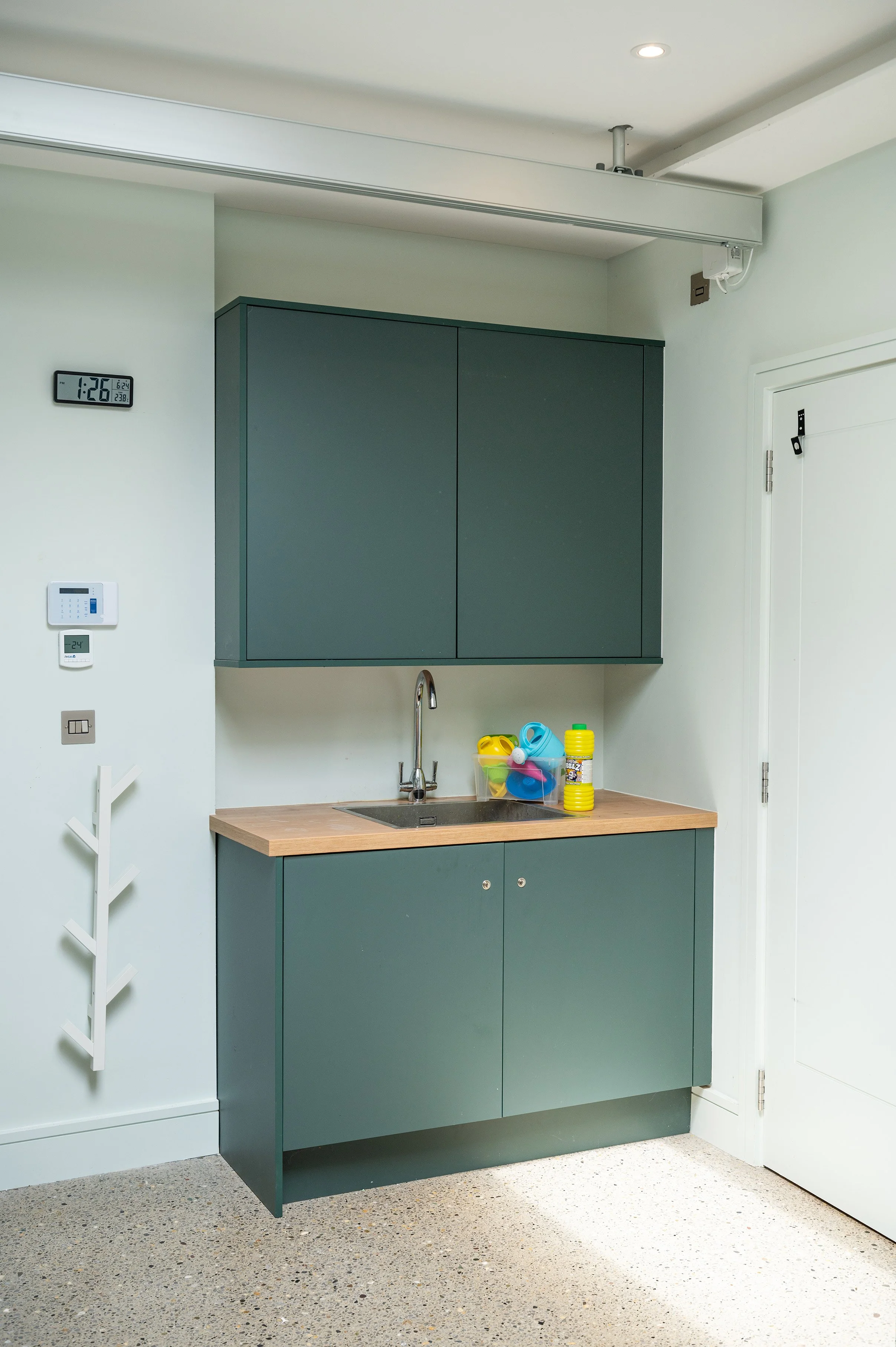 A room with a green kitchenette unit with a few water toys on the counter and a wall-mounted digital clock on the wall.