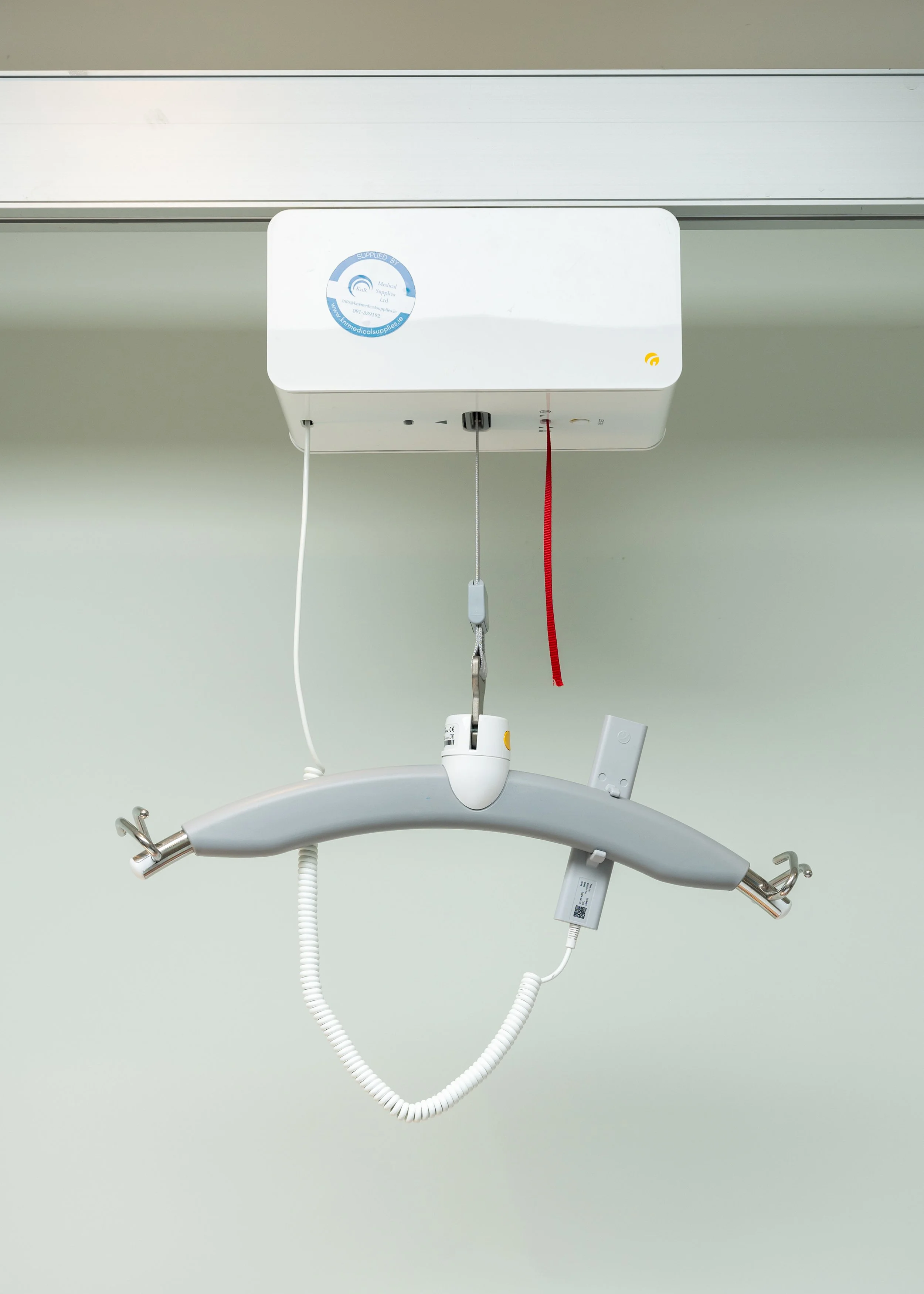 Overhead ceiling hoist with lifting bar and control unit, mounted on a wall track.
