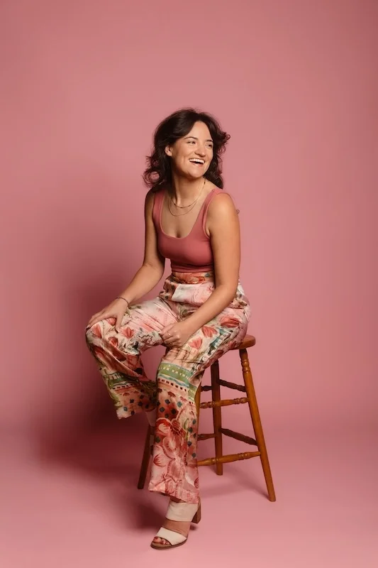 Kelsey Faye smiling with a pink background.