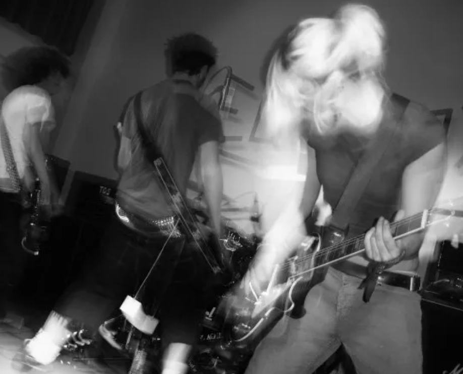 A black and white photo of Hannah as a teenager, playing high energy guitar in an emo-punk band
