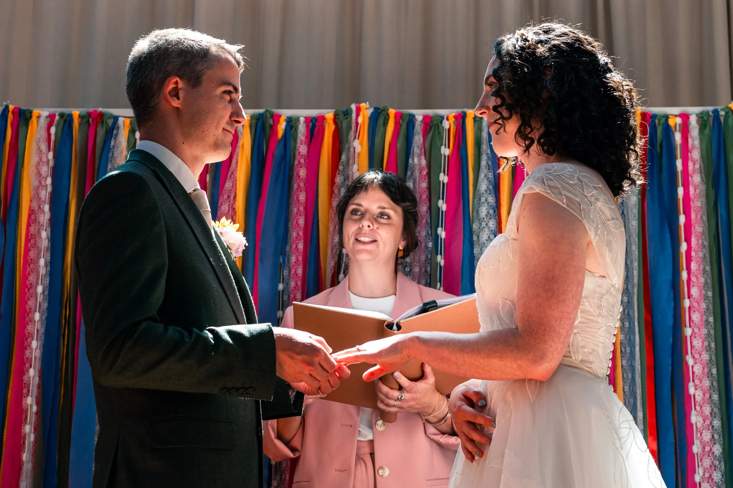 Hannah stands with a cis-het couple as they exchange rings at their wedding