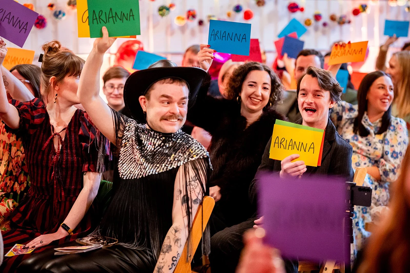 A crowd of eccentric and colourful people are laughing and holding up signs during a wedding