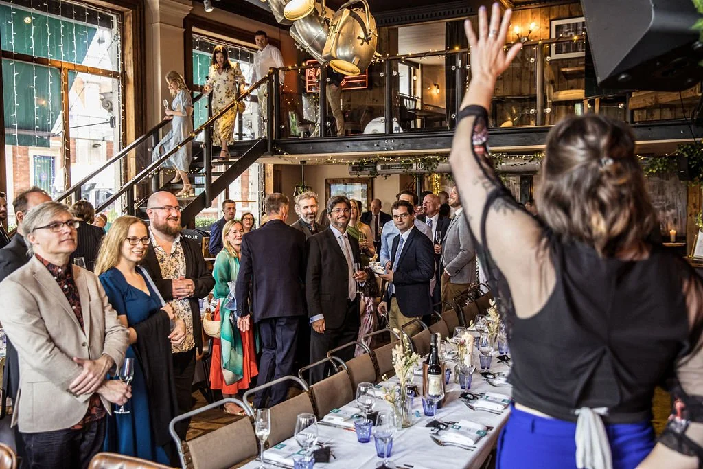 Hannah has her hand in the air and is getting the attention of a large room of people