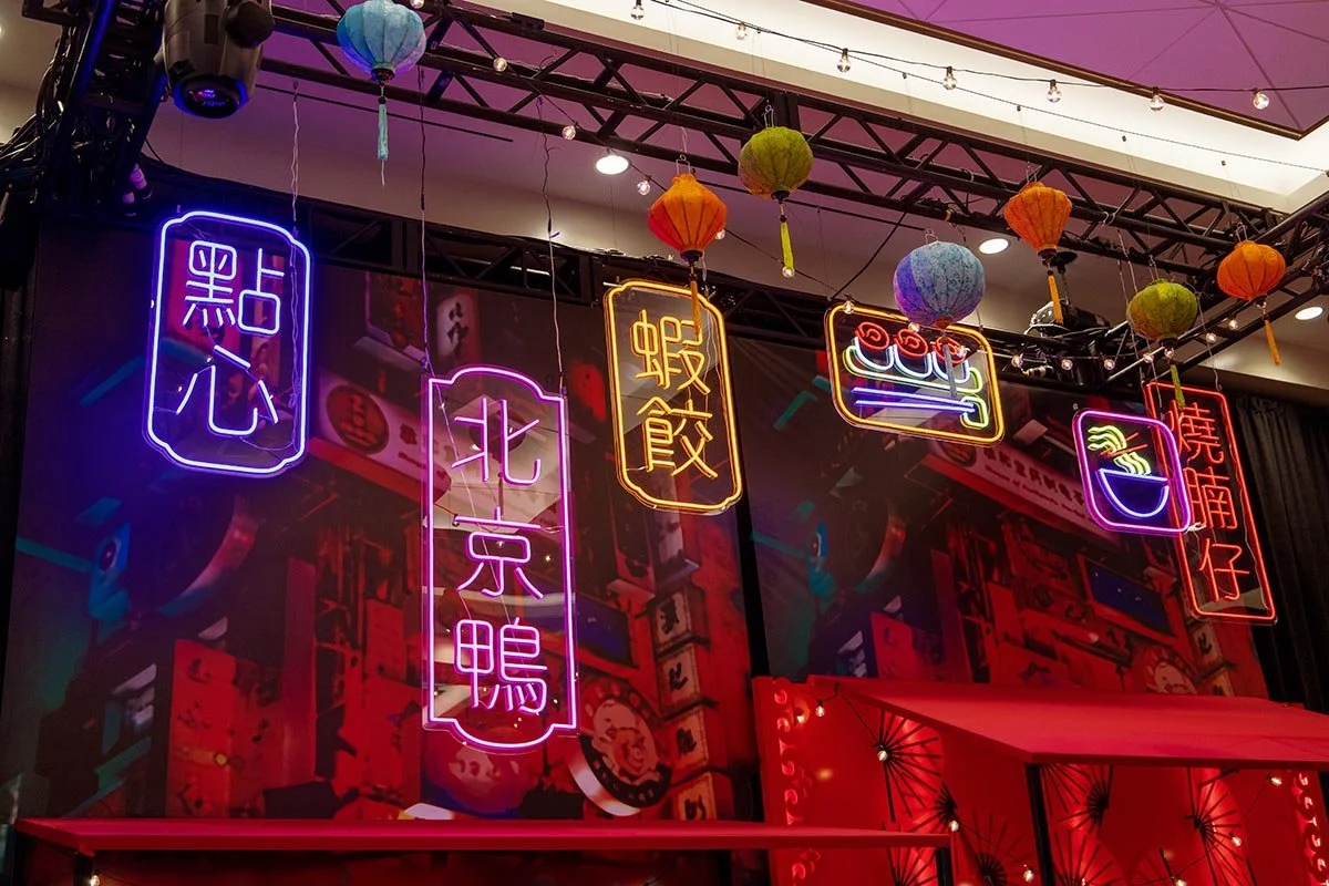 Colorful neon signs with Chinese characters, decorated with hanging paper lanterns in various colors, inside a lively restaurant or cafe.