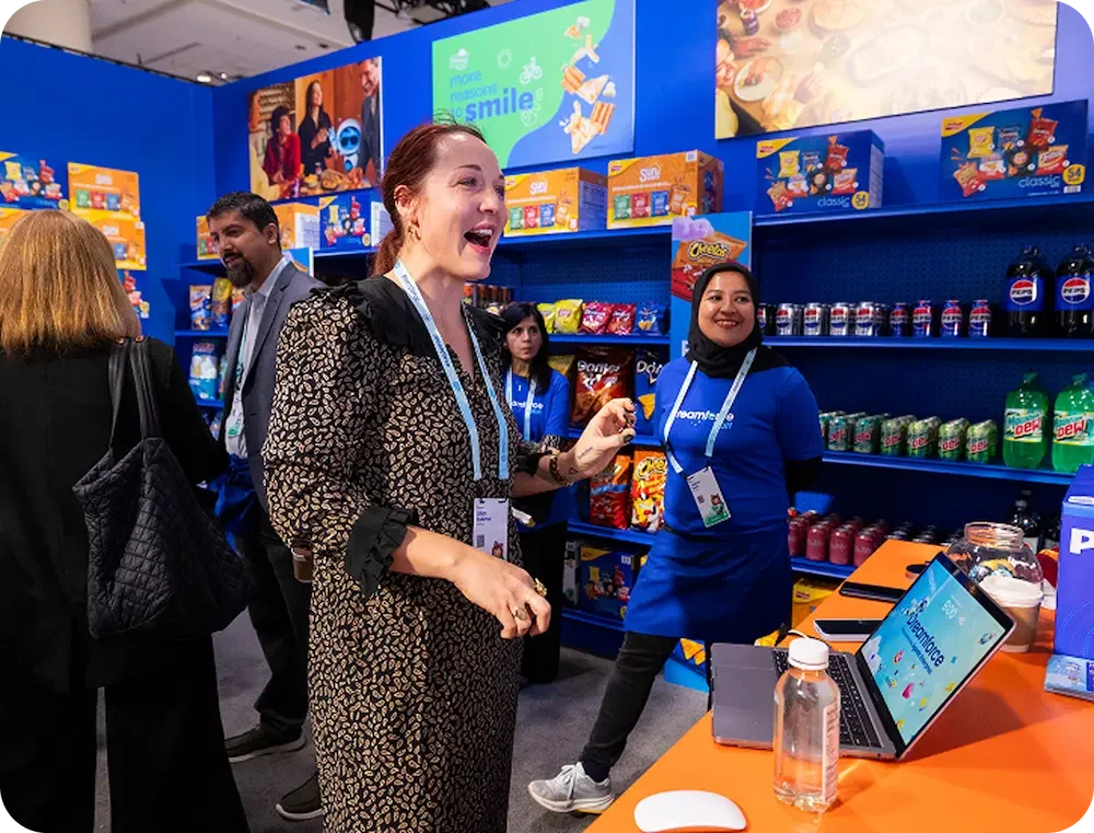 Business professionals at a trade show booth with snack displays and a computer.