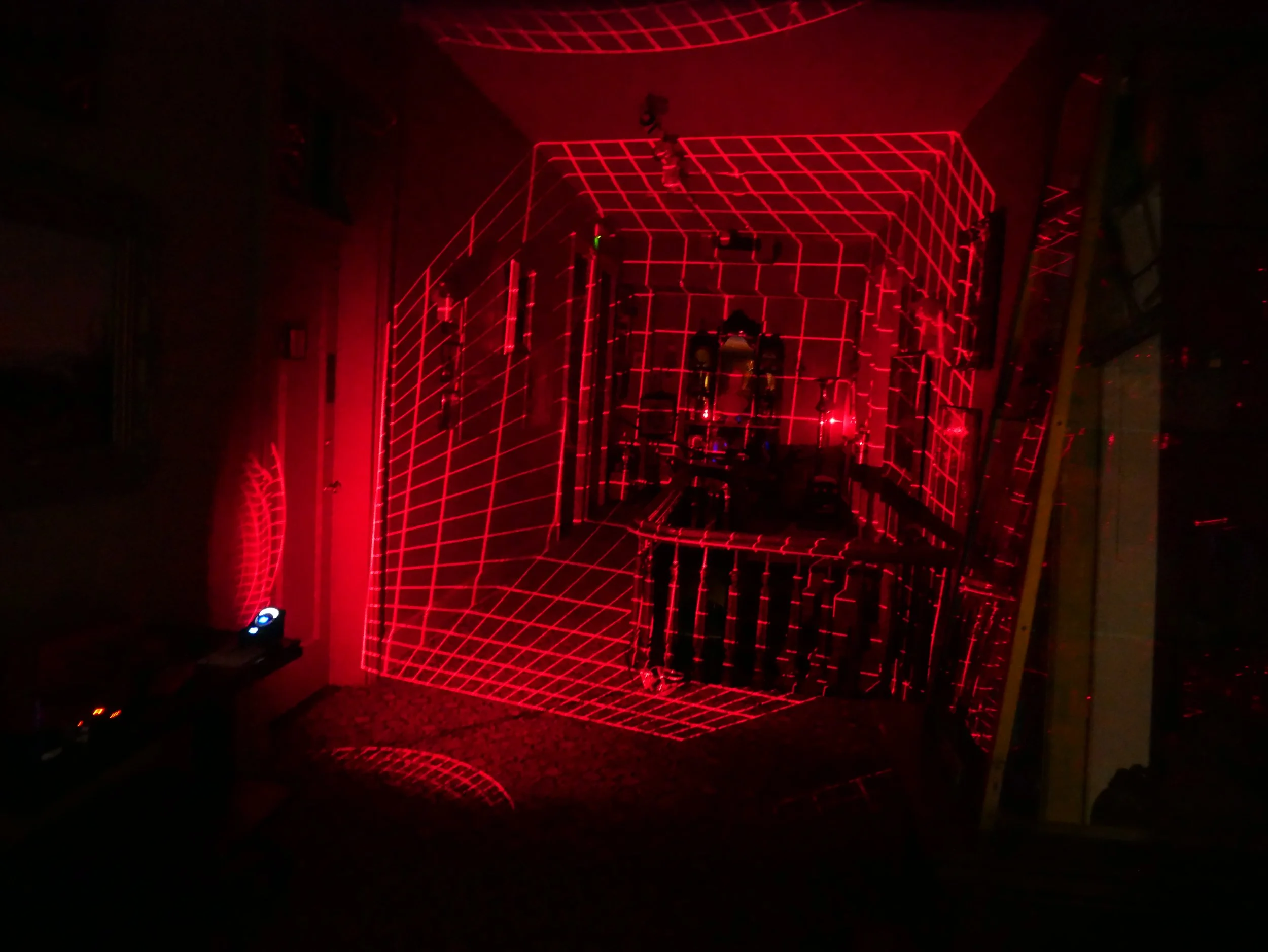 A dark room with a glowing 3D geometric wireframe structure illuminated in red laser lights, creating a futuristic pattern.